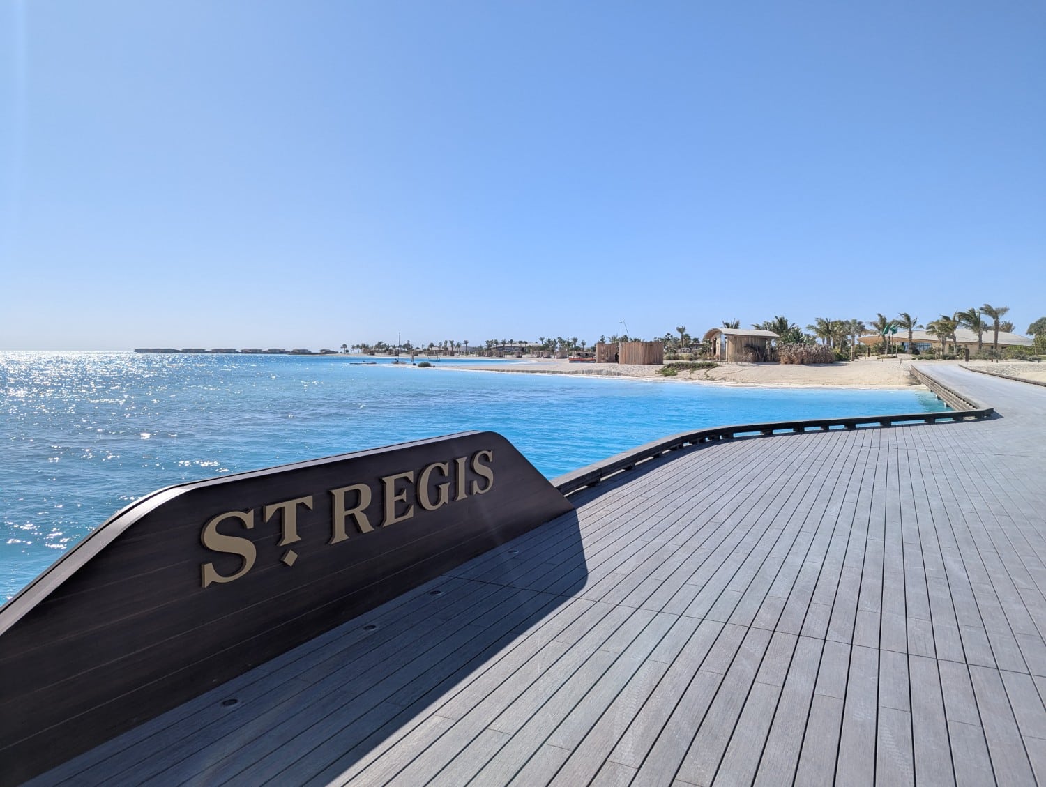 St Regis Red Sea Resort sign on the dock with beach in the background.