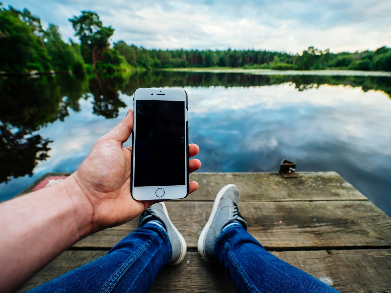 person with cellphone sitting by lake