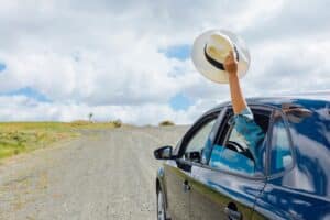 car driving down road with person in backseat with arm out of window