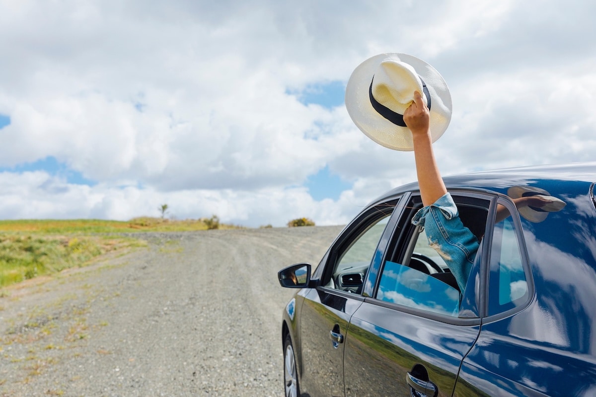 car driving down road with person in backseat with arm out of window